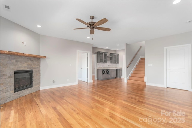 unfurnished living room with stairs, light wood finished floors, a fireplace, and visible vents