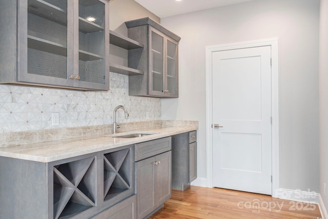 kitchen with a sink, decorative backsplash, light stone countertops, open shelves, and glass insert cabinets