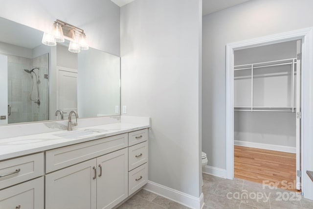 full bathroom with tile patterned flooring, vanity, baseboards, a shower stall, and a walk in closet