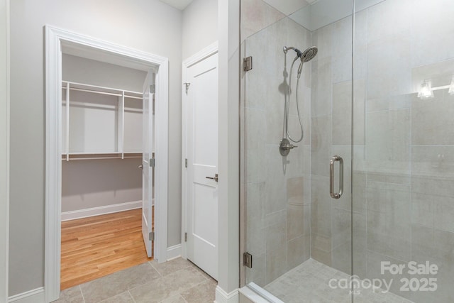 bathroom with a spacious closet, wood finished floors, a shower stall, and baseboards