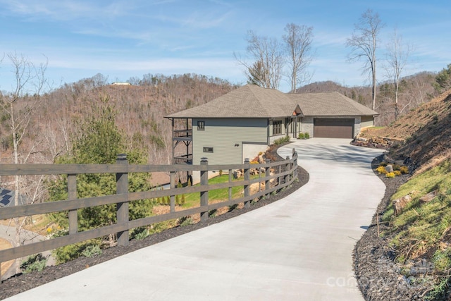 view of property exterior with a garage, concrete driveway, fence, and a view of trees