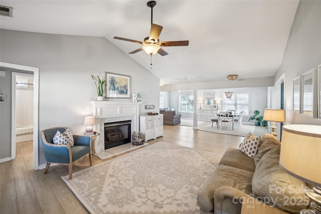 living area with ceiling fan, vaulted ceiling, a premium fireplace, and wood finished floors