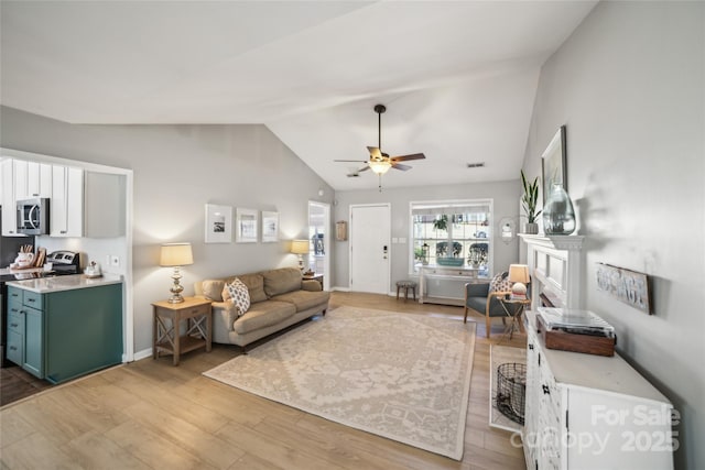 living room featuring visible vents, a ceiling fan, vaulted ceiling, light wood-type flooring, and a fireplace