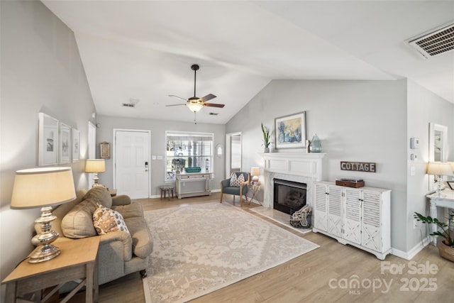 living area with vaulted ceiling, light wood finished floors, a fireplace with flush hearth, and visible vents