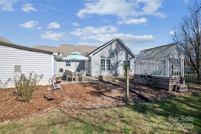 back of house featuring a greenhouse, an outdoor structure, fence, and a patio