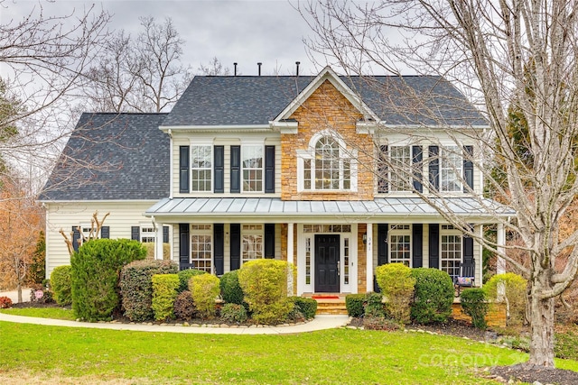 colonial home featuring roof with shingles, a front yard, a standing seam roof, metal roof, and stone siding