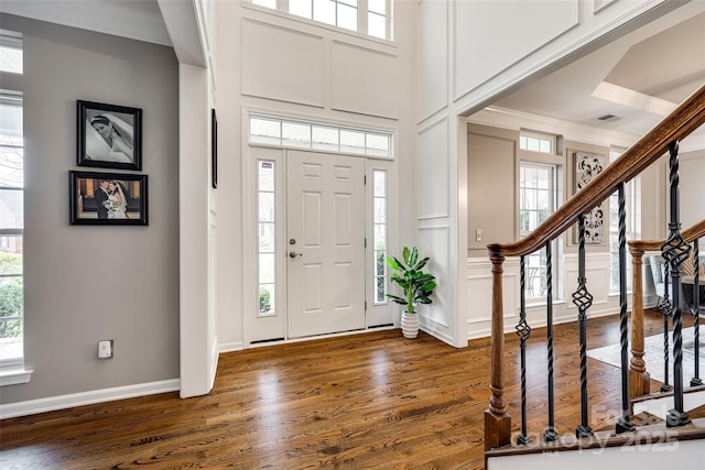 entrance foyer with ornamental molding, dark wood-style flooring, a decorative wall, and a high ceiling