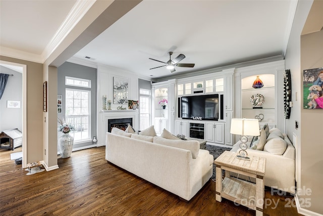 living area with crown molding, a fireplace, visible vents, dark wood-type flooring, and ceiling fan