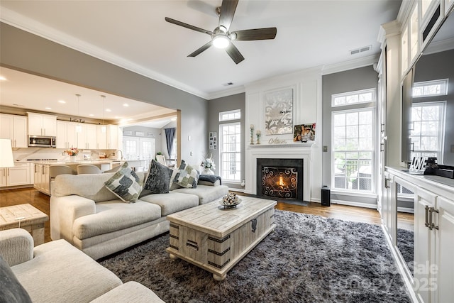 living area with recessed lighting, dark wood-style flooring, a fireplace with flush hearth, visible vents, and ornamental molding