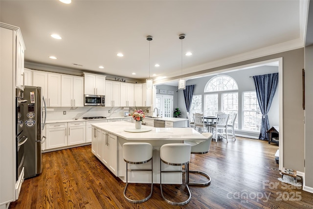 kitchen with light stone counters, a center island, decorative light fixtures, stainless steel appliances, and white cabinetry