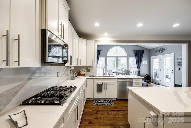 kitchen featuring a peninsula, light stone countertops, stainless steel appliances, and a sink