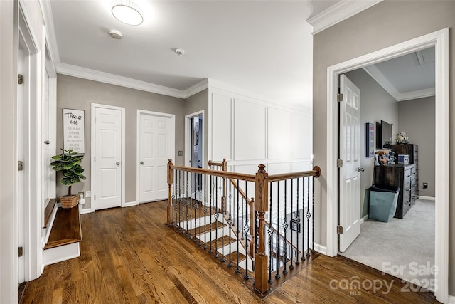 corridor with a decorative wall, dark wood finished floors, crown molding, and an upstairs landing