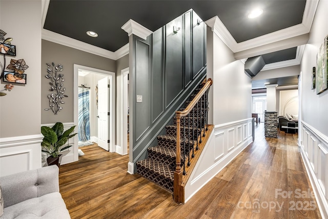 staircase featuring crown molding, a decorative wall, and wood finished floors