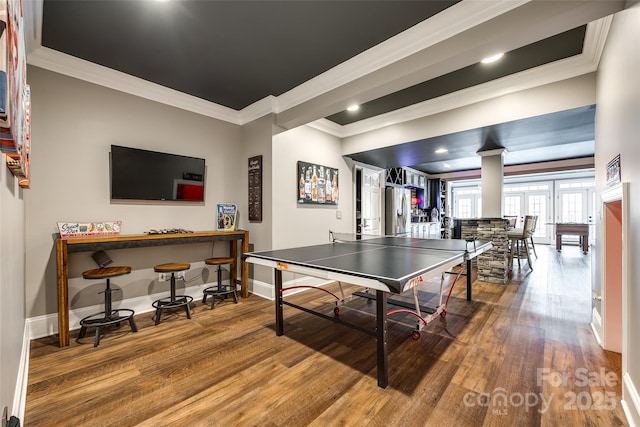 recreation room featuring decorative columns, baseboards, wood finished floors, crown molding, and a bar