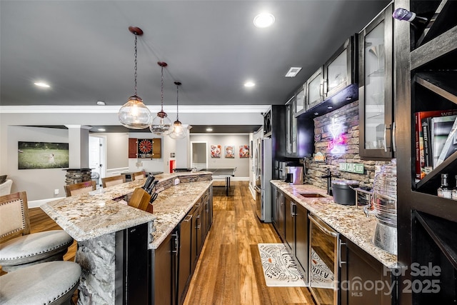 kitchen featuring a breakfast bar, a sink, a large island, light stone countertops, and pendant lighting