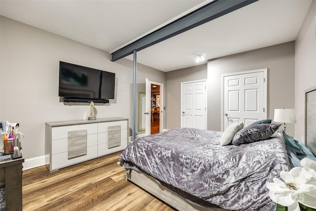 bedroom featuring beam ceiling, baseboards, and wood finished floors