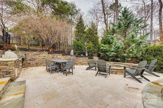 view of patio / terrace featuring an outdoor fire pit, fence, outdoor dining area, and exterior kitchen