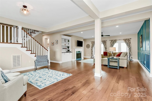 entrance foyer with wood finished floors, visible vents, baseboards, a fireplace with flush hearth, and stairs