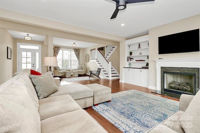 living area featuring a ceiling fan, wood finished floors, a fireplace, baseboards, and stairs