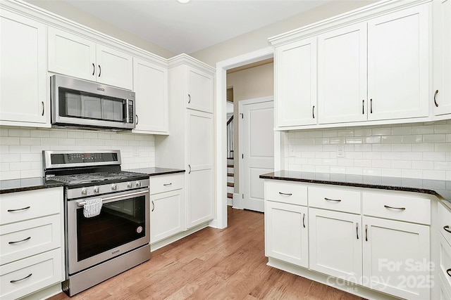 kitchen with dark stone countertops, white cabinets, light wood finished floors, and appliances with stainless steel finishes