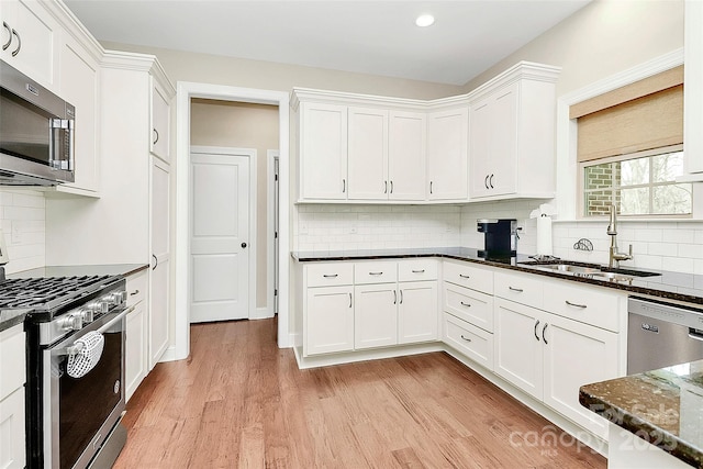 kitchen with light wood-type flooring, a sink, white cabinetry, dark stone counters, and appliances with stainless steel finishes