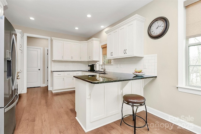 kitchen with stainless steel fridge with ice dispenser, a breakfast bar area, a peninsula, light wood-style floors, and white cabinets