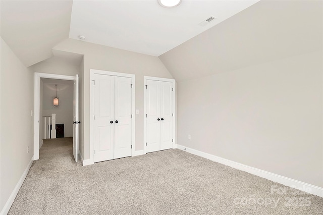 unfurnished bedroom with light carpet, visible vents, multiple closets, and vaulted ceiling