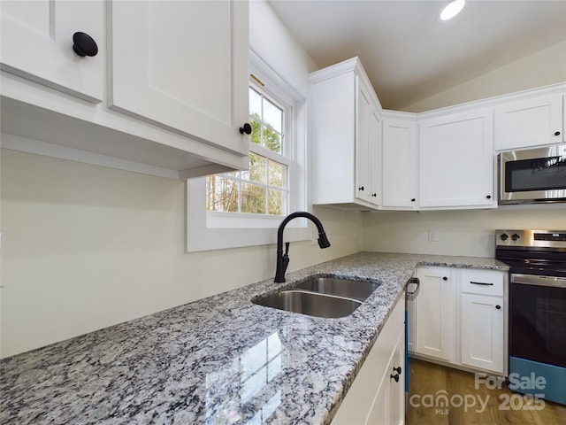 kitchen with appliances with stainless steel finishes, white cabinetry, vaulted ceiling, a sink, and light stone countertops