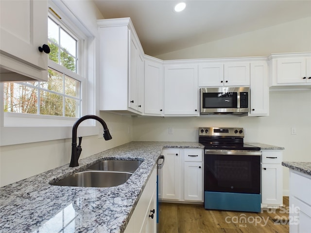 kitchen with lofted ceiling, light stone counters, a sink, white cabinetry, and appliances with stainless steel finishes