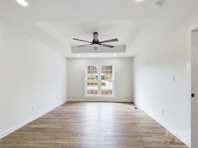 unfurnished room featuring light wood finished floors, recessed lighting, a raised ceiling, a ceiling fan, and baseboards