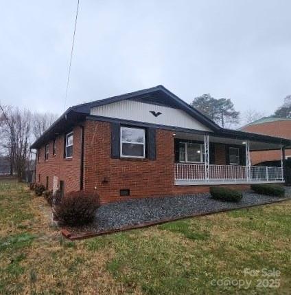 view of side of home featuring a yard, brick siding, crawl space, and a porch