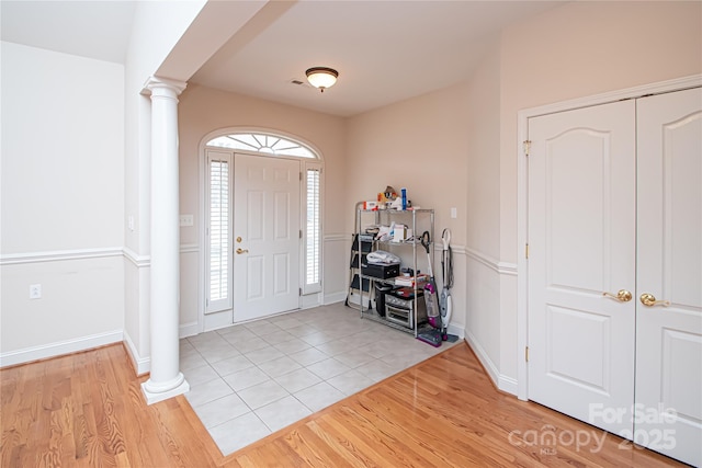 entryway with light wood-type flooring, decorative columns, and baseboards