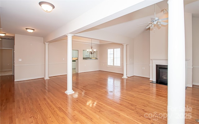 unfurnished living room with light wood-style floors, decorative columns, ceiling fan with notable chandelier, and a fireplace with flush hearth