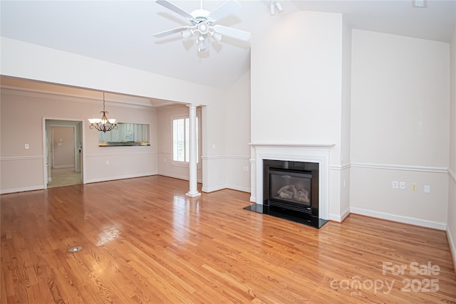 unfurnished living room with a glass covered fireplace, vaulted ceiling, light wood-type flooring, ornate columns, and ceiling fan with notable chandelier