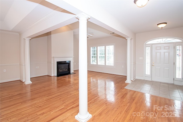 foyer entrance with light wood-type flooring, ornate columns, a fireplace with flush hearth, and baseboards