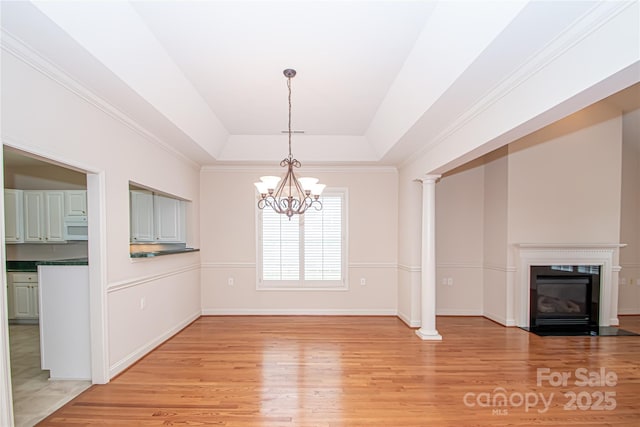 unfurnished dining area with a chandelier, a tray ceiling, a fireplace with flush hearth, and light wood-style floors