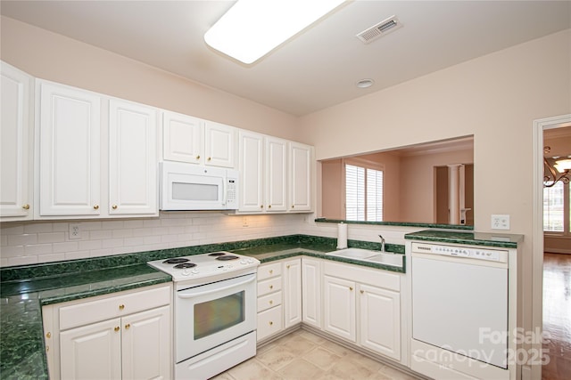 kitchen featuring dark countertops, visible vents, white cabinets, a sink, and white appliances