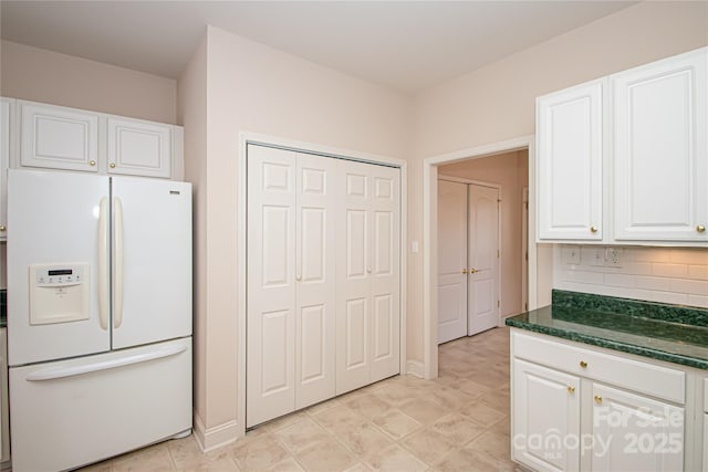 kitchen with white fridge with ice dispenser, dark stone counters, white cabinets, and tasteful backsplash