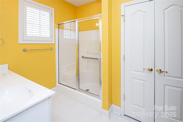 bathroom featuring double vanity, baseboards, tile patterned floors, a shower stall, and a sink