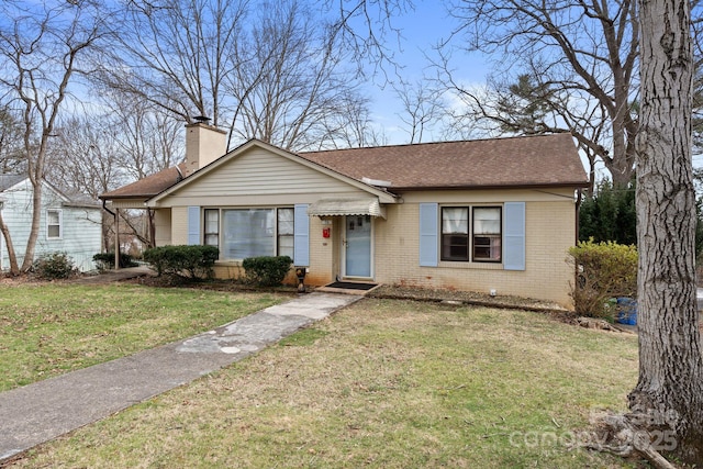 view of front of property featuring a shingled roof, a front yard, brick siding, and a chimney