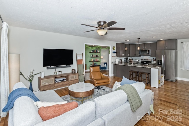 living area with light wood-style flooring, baseboards, ceiling fan, and a textured ceiling