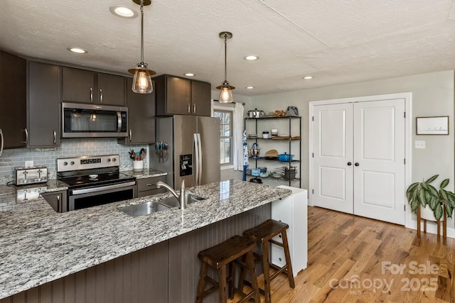 kitchen with dark brown cabinetry, appliances with stainless steel finishes, a peninsula, light stone countertops, and a sink