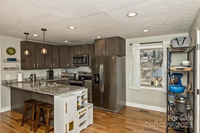 kitchen featuring stainless steel appliances, a peninsula, a sink, dark brown cabinets, and open shelves