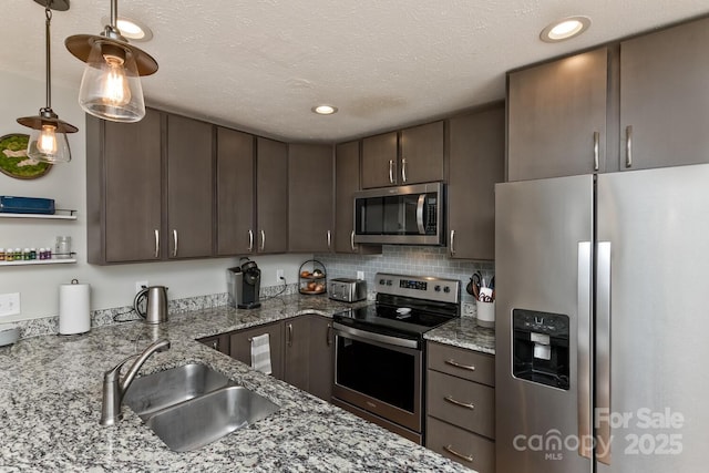 kitchen featuring hanging light fixtures, appliances with stainless steel finishes, dark brown cabinetry, a sink, and light stone countertops