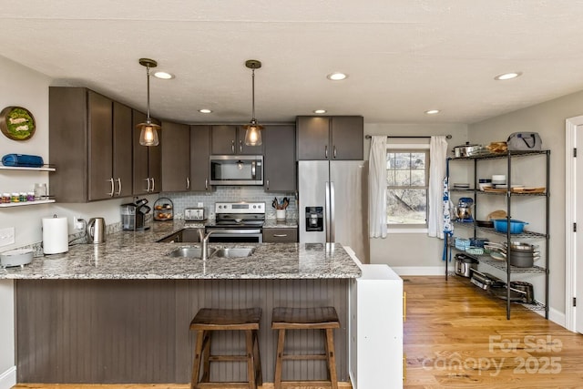 kitchen with stainless steel appliances, dark brown cabinetry, a peninsula, and light stone countertops