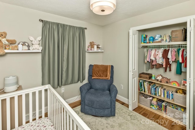 bedroom with a crib, baseboards, a closet, and wood finished floors