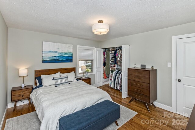 bedroom featuring a textured ceiling, a closet, wood finished floors, and baseboards