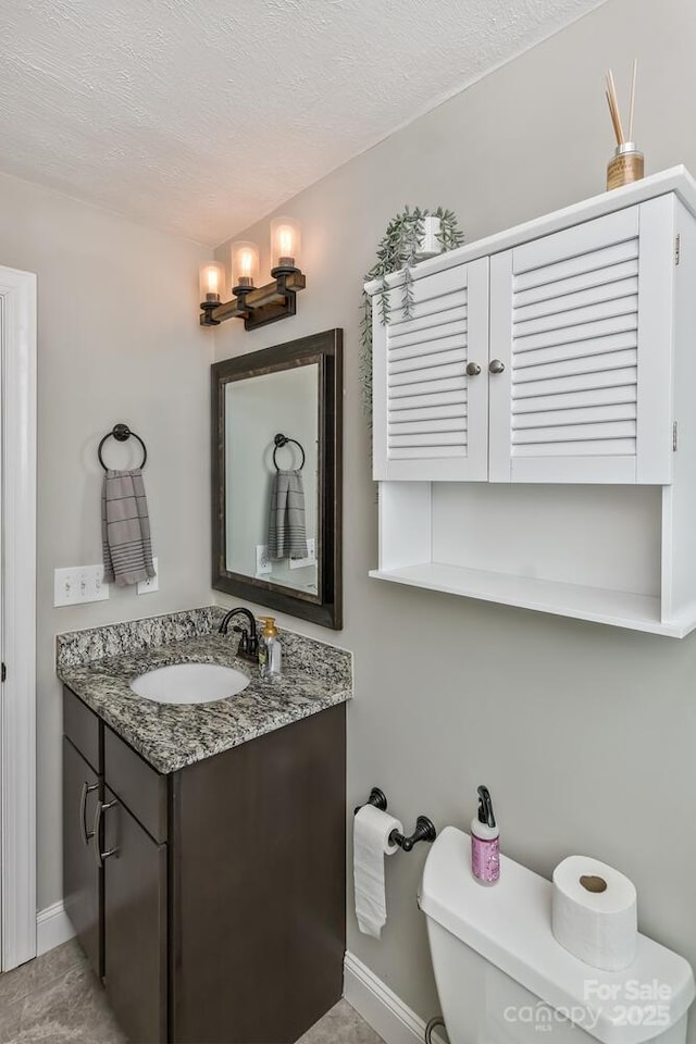 half bathroom with a textured ceiling, toilet, vanity, and baseboards