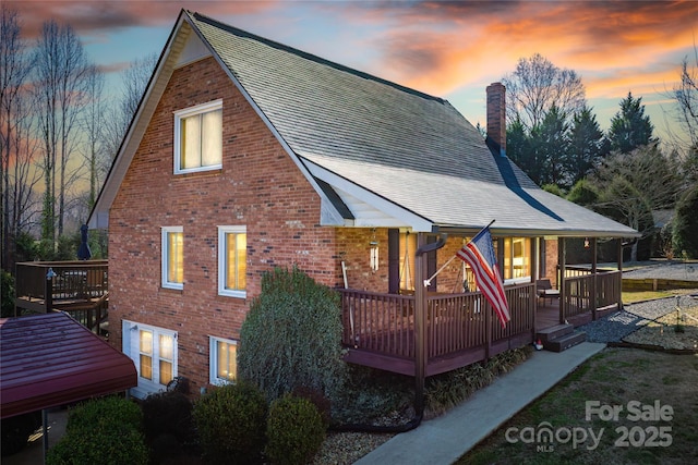 back of house with a deck, brick siding, and a chimney