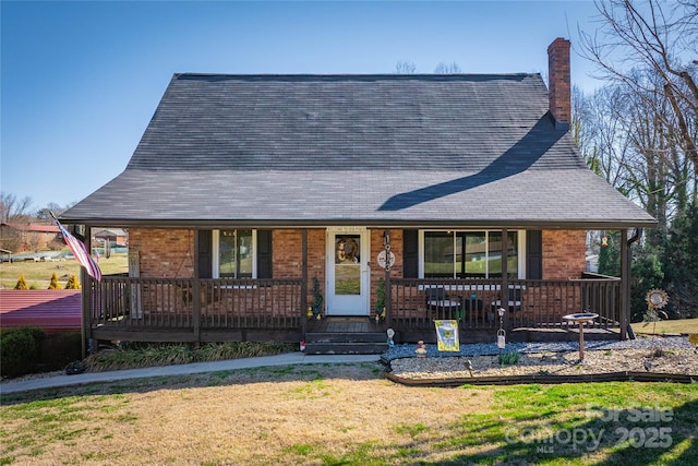 view of front of house with a porch, a chimney, a front yard, and brick siding